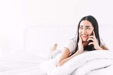Rahatlatıcı ve home.woman, yatağa smartphone kullanarak mutlu kadın konuşmak smartphone ile
