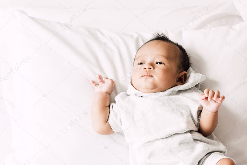 Portrait of baby relaxing on white bed in room