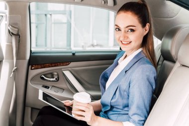 İşkadını lüks araba koltuğunda dijital tablet bilgisayar ve arkada kahve fincan holding ile çalışma