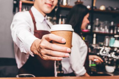 Bir tezgahın arkasındaki yakışıklı barista ayakta ve müşteri kafede kahve fincanı verilmesi