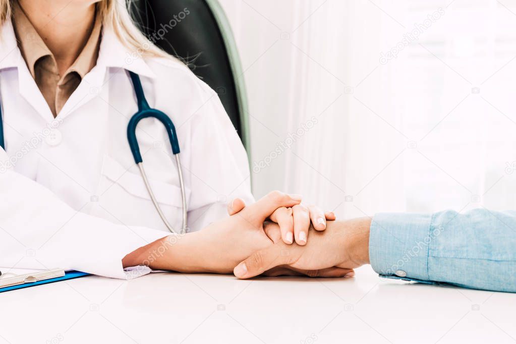 Female doctor consulting and holding hand male patient reassuring with care on doctors table in hospital.healthcare and medicine