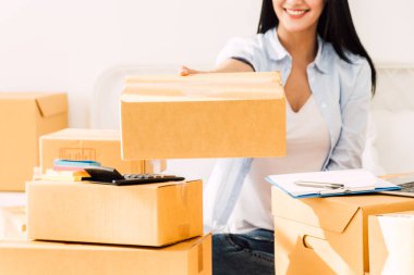 Çalışma ve karton tutan genç kadın serbest meslek sahibi KOBİ iş online ve teslimat kavramı kutu yatağa evde -