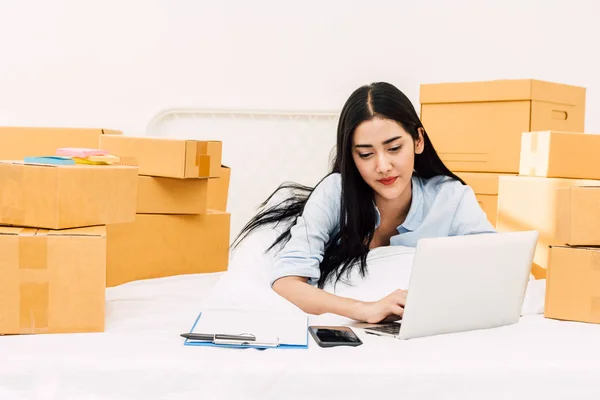 年轻女子自由职业者工作和使用笔记本电脑与纸板盒在家里的床上 中小企业业务在线和交付概念 — 图库照片