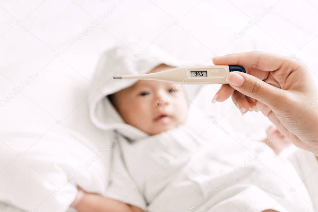 Mother holding thermometer of her ill baby.Sick baby on bed with fever measuring temperature