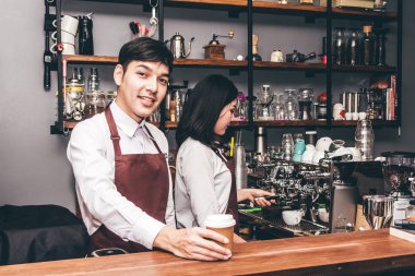 Bir tezgahın arkasındaki yakışıklı barista ayakta ve müşteri kafede kahve fincanı verilmesi