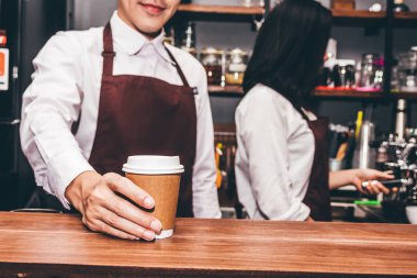 Bir tezgahın arkasındaki yakışıklı barista ayakta ve müşteri kafede kahve fincanı verilmesi