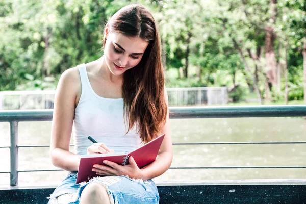 Kadın evde oturan bir defter üzerinde yazma kalemi ile