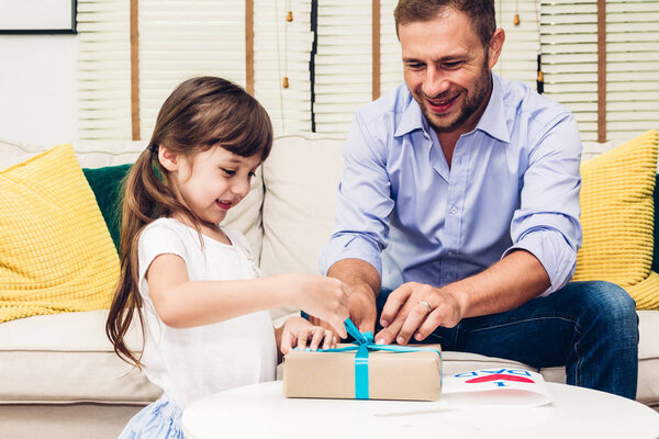 Little daughter giving her father a blue ribbon gift box for surprise at father's day.Love of family and father day concept