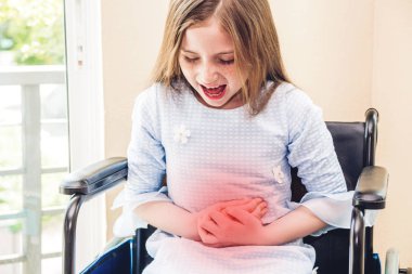 Küçük kız mide ağrısı acı ve tekerlekli hospital.sick sandalyede oturup küçük girl.healthcare ve Tıp