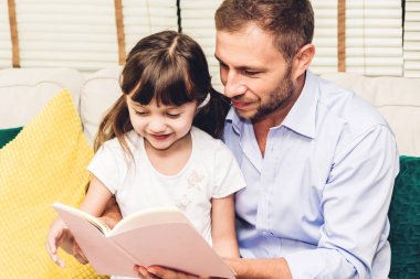 Babası ile eğleniyor ve evde kanepede birlikte kitap okumak küçük kızı. Küçük kız ve baba hikaye kitabı ile zevk. Aile sevgisi ve kavram