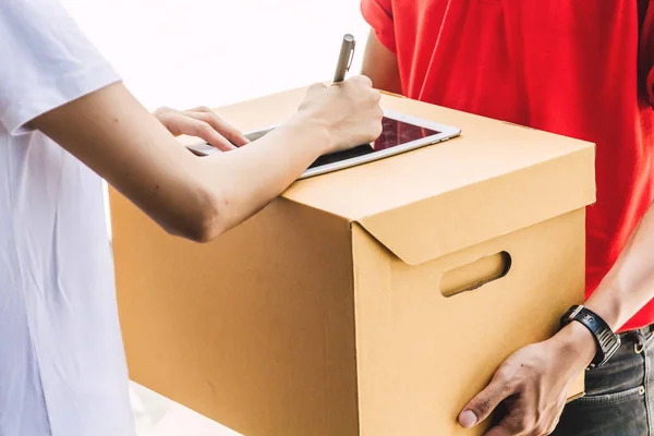 Woman putting signature in tablet on cardboard box to receiving package with delivery man in red uniform.courier service concept