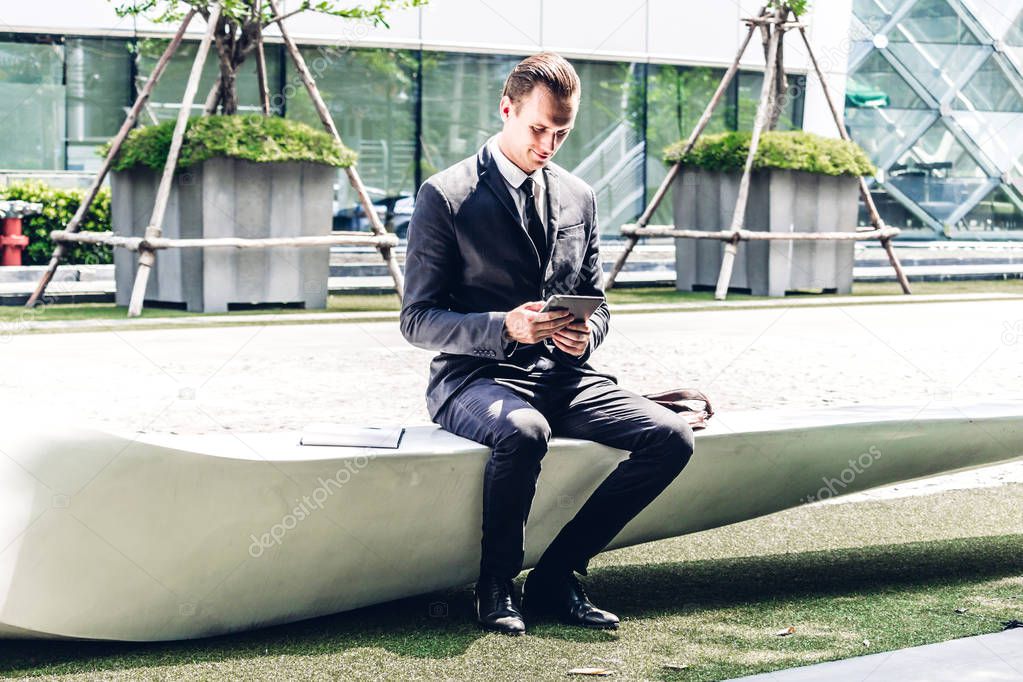 Handsome businessman in black elegant suit sitting and working with tablet computer on the city.Business and technology concept