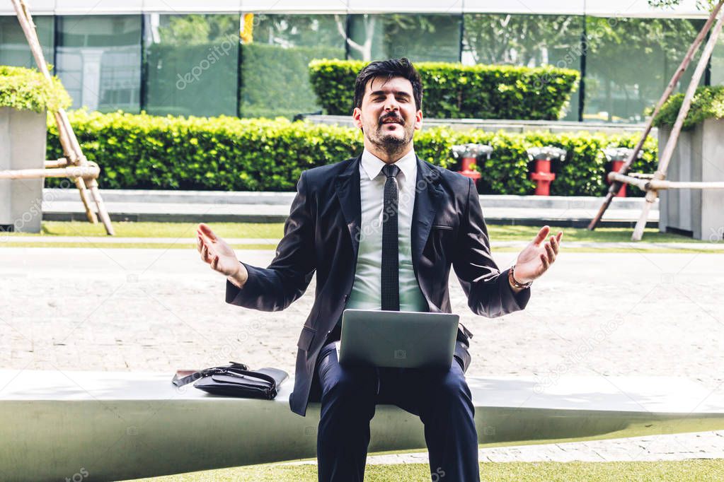 Handsome businessman in black elegant suit sitting and working with laptop computer.Man relax and enjoy with nature fresh air at city.Business and startup idea concept