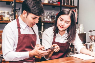 Gülümseyen ve bir kafede sayaç barın arkasında çalışan çift küçük işletme sahibi portresi. Barista smartphone kullanarak ve müşteriden sipariş almak