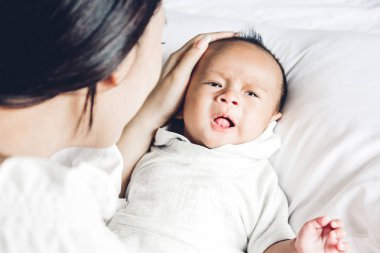 Beyaz bir yatak odasında kucağında bebek tutan anne. Aşk aile kavramının