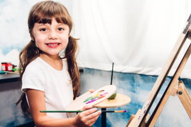 Little girl artist drawing on canvas with color palette and watercolor paints at home