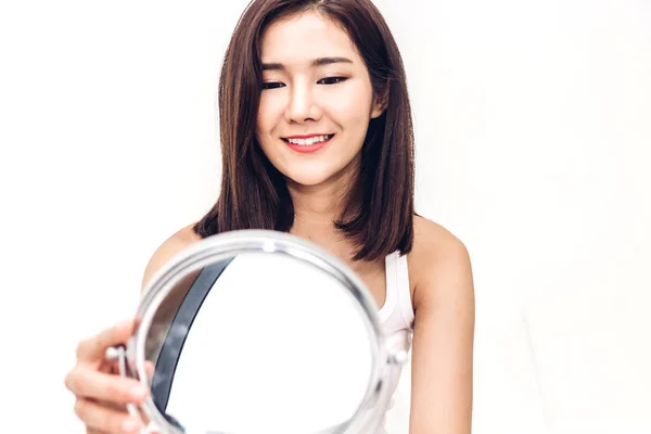 Smiling young beautiful asian woman fresh healthy skin looking on mirror at home.facial beauty and cosmetic concept