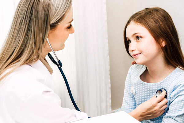 Врач осматривает маленькую девочку со стетоскопом в больнице.
