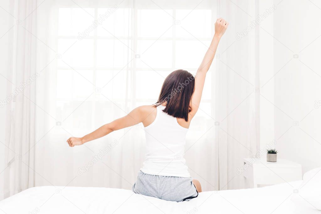 Woman sitting near the window and stretching in bed after wake up.Woman happy and relaxed breathing fresh air at morning