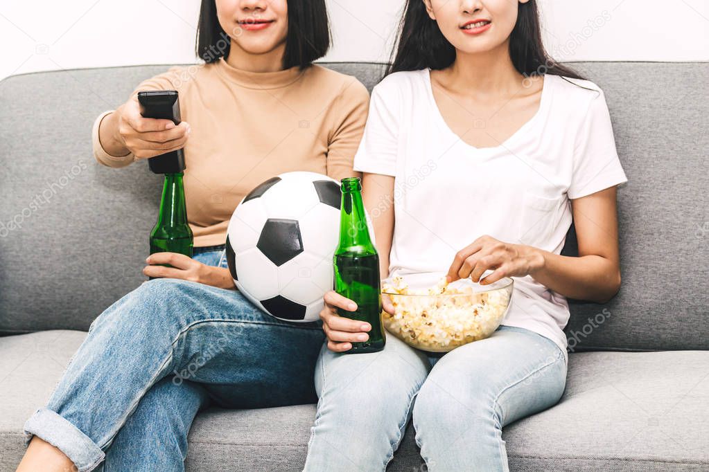 Two woman friends eating popcorn and drinking beer together and watching soccer game on sofa at home.Friendship and party concept