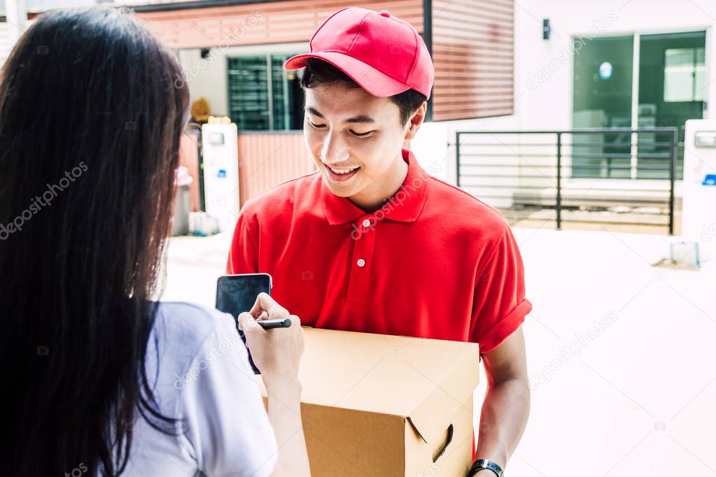 Woman putting signature on smartphone with cardboard box to receiving package with delivery man in red uniform.courier service concept