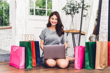 Güzel kadın shoping online dizüstü bilgisayar ve renkli alışveriş çantası yere evde oturmak teknoloji ile