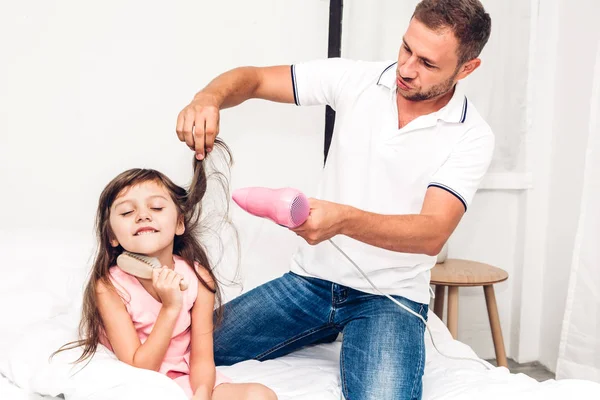 Father drying little daughter hair and playing together on the bed at home.Love of family and father day concept