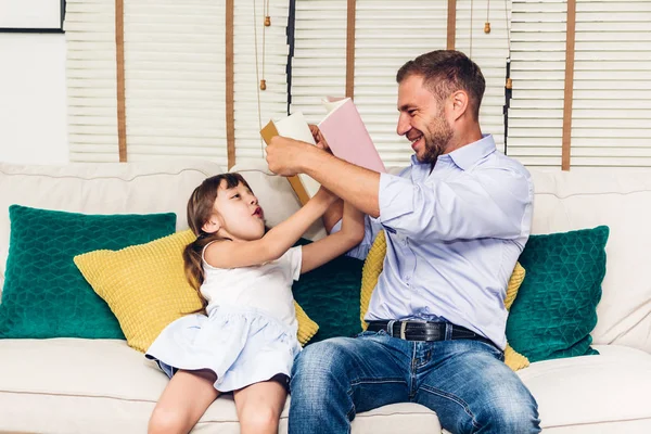 Father with little daughter having fun and read the book together on the sofa at home.Little girl and daddy enjoying with story book.Love of family and concept