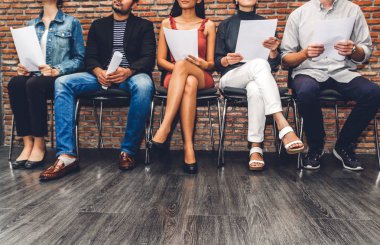 Group of business people holding paper while sitting on chair waiting for job interview against brick background clipart