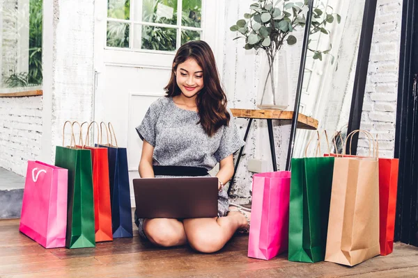 ラップトップ コンピューターや自宅の床に座ってカラフルなショッピング バッグの技術を持つ美しい女性ショッピングをオンライン — ストック写真