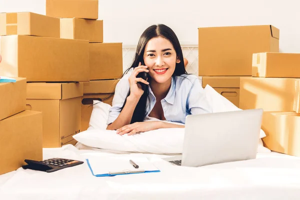 Genç kadın bağımsız çalışma ve kullanım dizüstü bilgisayar ile karton kutu yatağa evde - KOBİ iş online ve teslimat kavramı