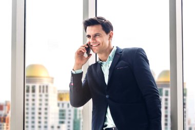 Siyah şık elbiseli işadamı çalışma ve modern ofis pencere yakınındaki şehir background.Communication konsepti üzerine konuşan akıllı telefon teknolojisini kullanıyor