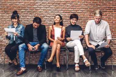 Group of business people holding paper while sitting on chair waiting for job interview against brick background clipart