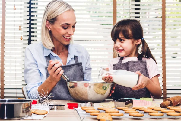 Mother and daugthter having fun cooking togather and learning to make a cake while baking in kitchen at home