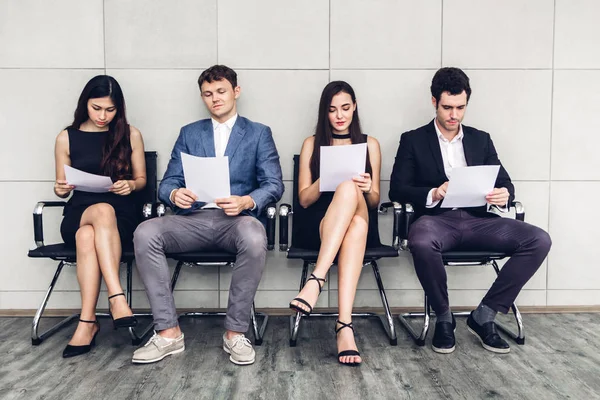 紙を押しながら壁の背景に就職の面接を待っている椅子に座っているビジネス人々 のグループ — ストック写真