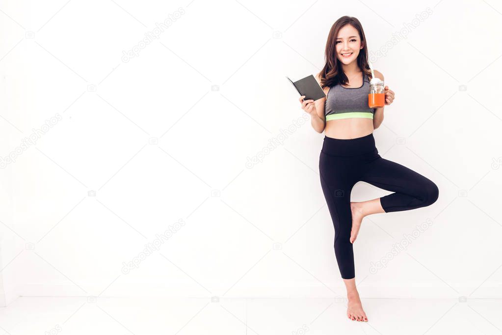 Sport woman in sportswear relax reading a book and drink fresh juice after workout against copy space for adding text with white wall background.Diet concept.Fitness and healthy lifestyle