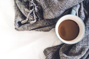 Bir fincan sıcak kahve ve beyaz yatakta sıcak eşarp. Kış ve soğuk hava kavramı