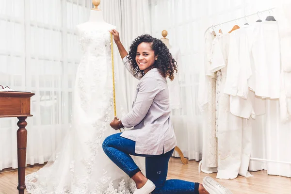 Gülümseyen Afro-Amerikan siyah kadın moda tasarımcısı atölye stüdyoda manken üzerinde elbise uygun çalışma ve kullanma teyp metre duruyor