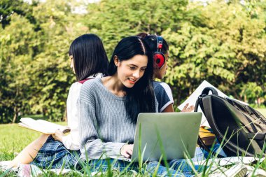 Bir grup gülümseyen uluslararası öğrenci veya genç dizüstü bilgisayarlarını kullanarak ödevlerini üniversitede parkta birlikte yapıyorlar. Eğitim ve arkadaşlık kavramı.