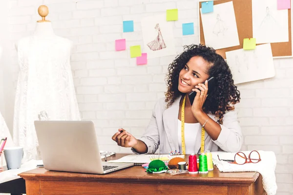 Smiling african american black woman fashion designer working with laptop computer at workshop studio