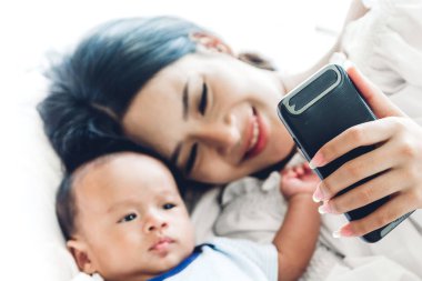 Anne ile bebek beyaz bir yatak odasında smartphone kullanın. Aşk aile kavramının
