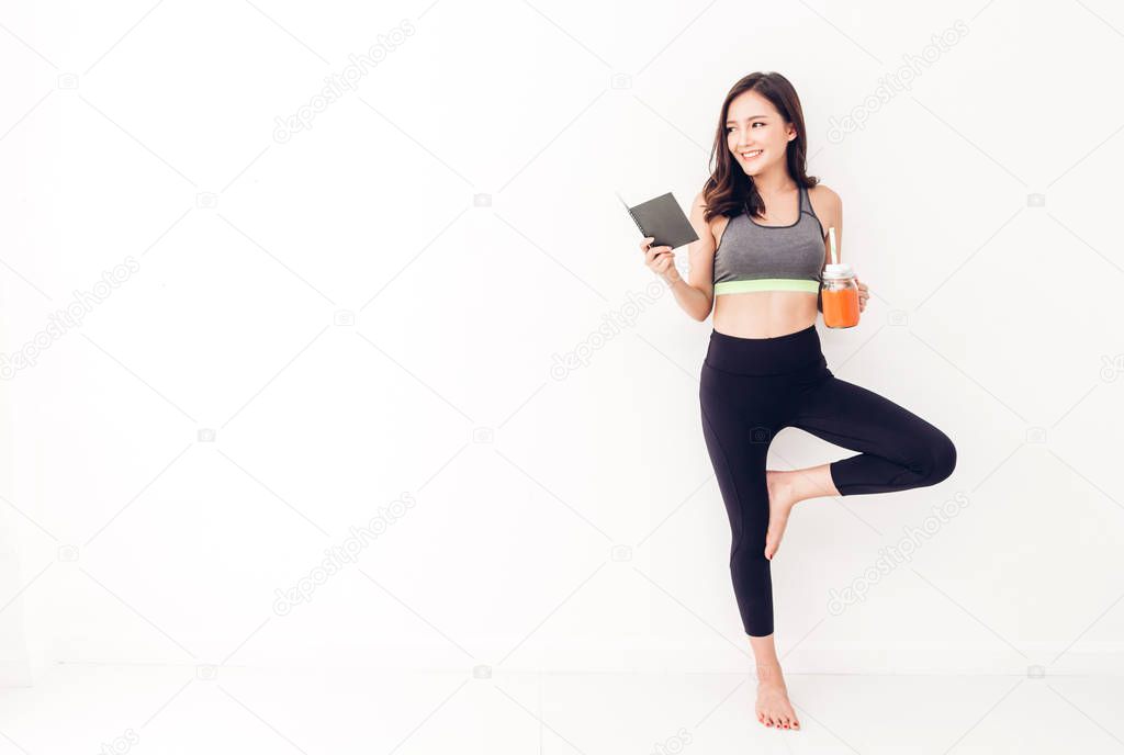 Sport woman in sportswear relax reading a book and drink fresh juice after workout against copy space for adding text with white wall background.Diet concept.Fitness and healthy lifestyle