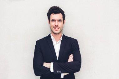 Yakışıklı gülümseyen iş adamı duvar arka plan üzerinde siyah takım elbise duran portresi