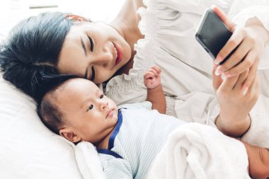 Anne ile bebek beyaz bir yatak odasında smartphone kullanın. Aşk aile kavramının