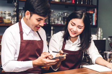 Gülümseyen ve bir kafede sayaç barın arkasında çalışan çift küçük işletme sahibi portresi. Barista smartphone kullanarak ve müşteriden sipariş almak