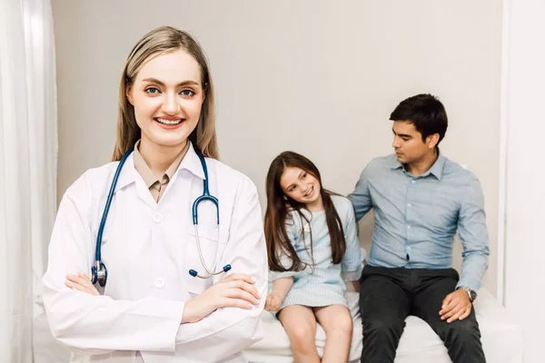 Doctor looking at camera while young family father and little girl  on background together