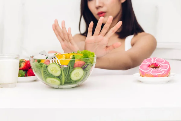 Woman making choice between healthy salad and calorie bomb chocolate donut.Woman rejecting with salad at home.Healthy eating diet and Junk food concept