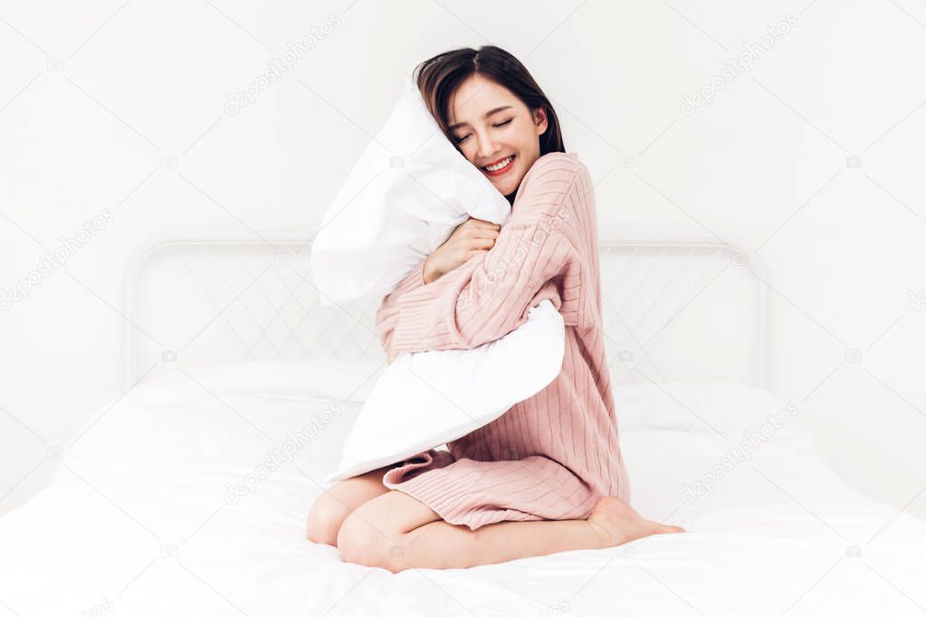 Beautiful woman smiling to camera and relaxing with pillow on the bed in her room at home