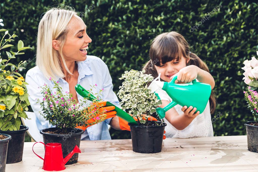 Mother with little daughter having fun and planting flowers in pot with soil together,daughter taking care of flower with watering plants in garden at home