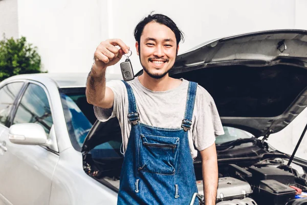 Professional car mechanic in uniform holding car key and fixing